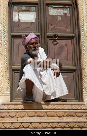 Man wearing a turban sits on his haunches on the top step, framed by the doorway. Stock Photo