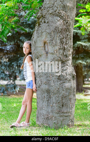 The girl stands near a thick tree in park Stock Photo