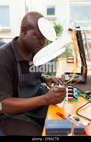 senior African technician repairing a circuit board under electronic magnifying glass
