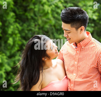 Horizontal photo of young Adult couple looking at each other with blurred green trees during daylight in background Stock Photo
