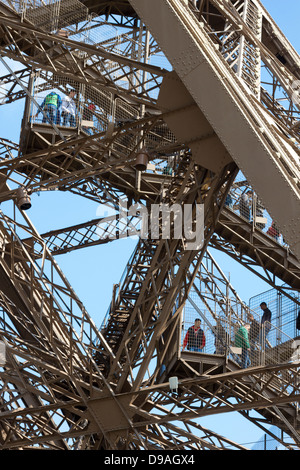 Tourists walking down steps through complex lattice iron girders to descend from first level of Eiffel Tower in Paris Stock Photo