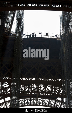 Silhouette of people looking out from first level platform of Eiffel Tower surrounded by decorative ironwork Stock Photo