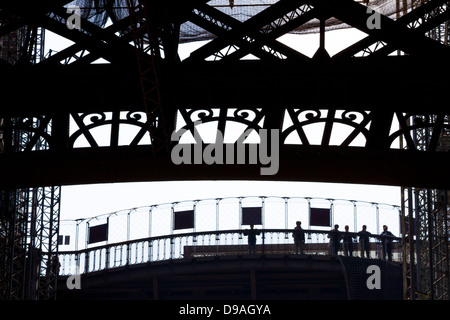 Silhouette of people looking out from first level platform of Eiffel Tower surrounded by decorative ironwork Stock Photo