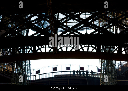 Silhouette of people looking out from first level platform of Eiffel Tower surrounded by decorative ironwork Stock Photo