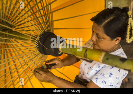 June 14, 2013 - Pathein, Ayeyarwady, Union of Myanmar - A worker strings an umbrella at the Shwe Sar umbrella factory in Pathein. Pathein is a center of the Burmese umbrella and parasol industry. Most are actually parasols made in the traditional Burmese way using treated paper which is not water proof. Shwe Sar's umbrella's are made with treated cloth and are waterproof. Since US and European sanctions have been lifted businesses in Myanmar have seen an explosion in exports. Shwe Sar exports most of their umbrellas to Europe. Pathein, sometimes also called Bassein, is a port city and the capi Stock Photo