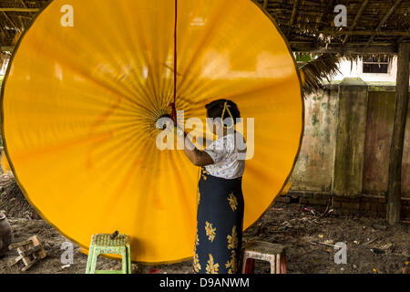 June 14, 2013 - Pathein, Ayeyarwady, Union of Myanmar - A worker strings an umbrella at the Shwe Sar umbrella factory in Pathein. Pathein is a center of the Burmese umbrella and parasol industry. Most are actually parasols made in the traditional Burmese way using treated paper which is not water proof. Shwe Sar's umbrella's are made with treated cloth and are waterproof. Since US and European sanctions have been lifted businesses in Myanmar have seen an explosion in exports. Shwe Sar exports most of their umbrellas to Europe. Pathein, sometimes also called Bassein, is a port city and the capi Stock Photo