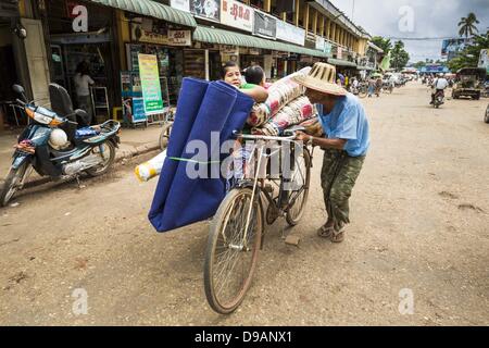 June 14, 2013 - Pathein, Ayeyarwady, Union of Myanmar - A pedicab pushes a fare up the road in the market in Pathein. Pathein is a center of the Burmese umbrella and parasol industry. Most are actually parasols made in the traditional Burmese way using treated paper which is not water proof. Shwe Sar's umbrella's are made with treated cloth and are waterproof. Since US and European sanctions have been lifted businesses in Myanmar have seen an explosion in exports. Shwe Sar exports most of their umbrellas to Europe. Pathein, sometimes also called Bassein, is a port city and the capital of the A Stock Photo