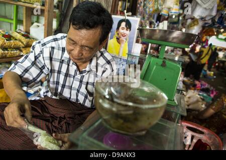 June 14, 2013 - Pathein, Ayeyarwady, Union of Myanmar - A market vendor with a photo of Burmese democracy icon, Aung San Suu Kyi in his shop, prepares an order in the market in Pathein. Pathein is a center of the Burmese umbrella and parasol industry. Most are actually parasols made in the traditional Burmese way using treated paper which is not water proof. Shwe Sar's umbrella's are made with treated cloth and are waterproof. Since US and European sanctions have been lifted businesses in Myanmar have seen an explosion in exports. Shwe Sar exports most of their umbrellas to Europe. Pathein, so Stock Photo