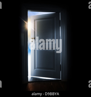 Opening blue door in a dark room with shining light and sky outside Stock Photo