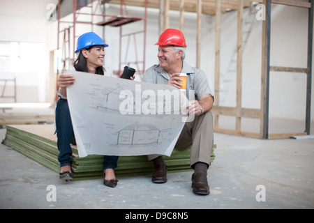 Male and female construction workers sitting down holding coffee and a blueprint Stock Photo