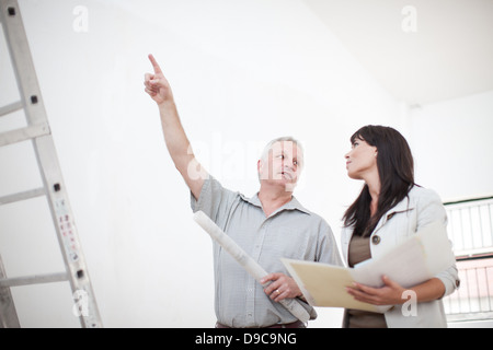 Male and female talking and pointing upwards holding blueprints next to ladders Stock Photo