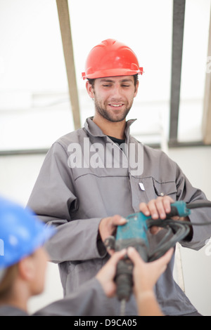 Male and female laborer handing electric drill on construction site Stock Photo