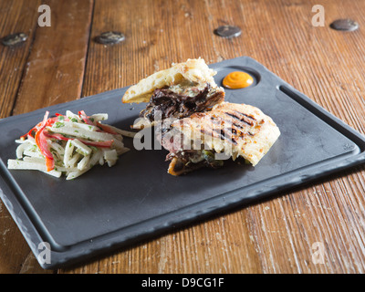 Rare gourmet grilled steak panini with Gorgonzola cheese served with colorful coleslaw on cast iron plate Stock Photo