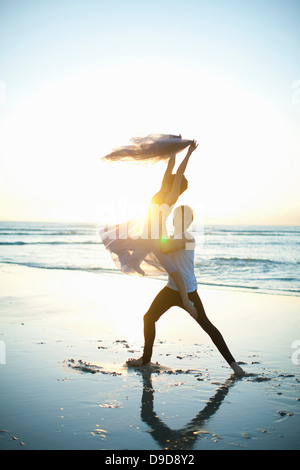 Young man lifting dancing partner on sunlit beach Stock Photo