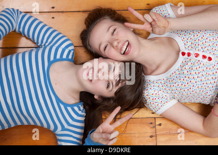 Girls lying on wooden floor doing peace signs Stock Photo