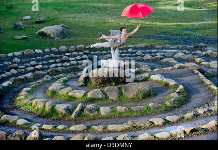 Mid adult dancers performing with red umbrellas in stone circle Stock Photo