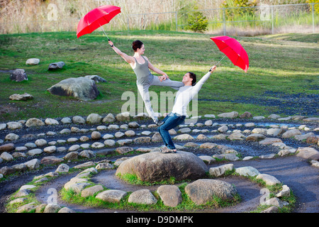 Mid adult dancers performing with red umbrellas in stone circle Stock Photo