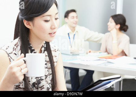 Woman holding mug, colleagues in background Stock Photo