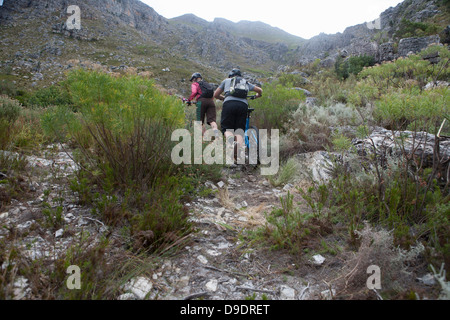 Young couple pushing mountain bikes up mountain Stock Photo