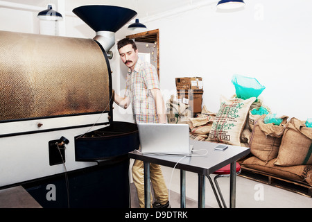 Coffee shop owner at work, using coffee roaster and laptop Stock Photo