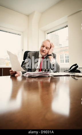 Senior businessman at desk with paperwork and head in hands Stock Photo