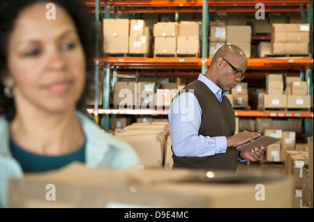 Male warehouse manager using digital tablet, woman in foreground Stock Photo