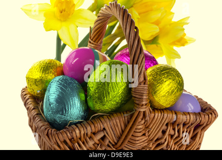 Small wicker basket with Easter eggs and daffodils isolated on white. Stock Photo