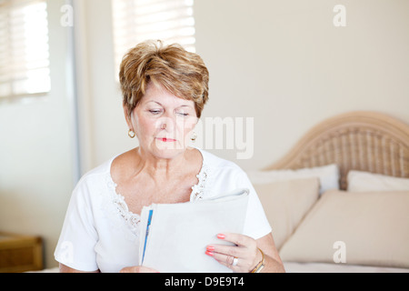 senior woman sitting on bed and reading newspaper Stock Photo