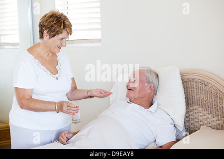 caring senior wife giving medicine to ill husband Stock Photo