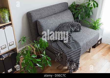Living room with bright green plants, bookshelf and gray armchair. Stock Photo