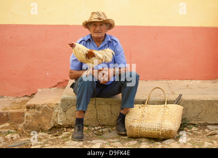 Local man wearing straw hat with cockerel standing on his knee, Trinidad, Cuba, West Indies Stock Photo