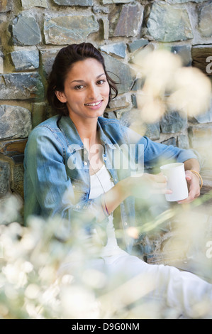 Portrait of a smiling woman leaning against a wall and drinking coffee Stock Photo