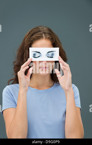 Woman hiding behind paper with false eyes Stock Photo