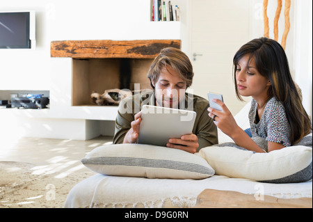 Couple lying on the bed and using electronic gadgets Stock Photo