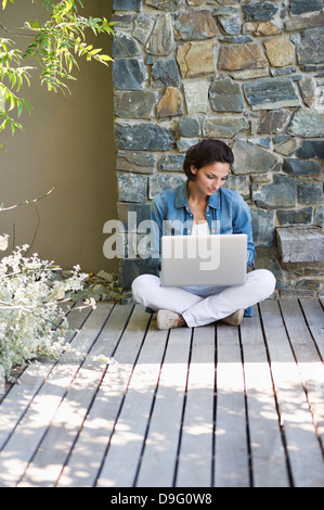 Woman sitting on a hardwood floor and using a laptop Stock Photo