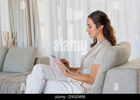 Beautiful woman using a digital tablet and smiling on a couch Stock Photo