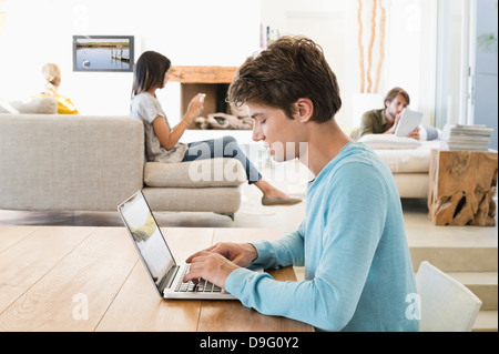 Man using a laptop with his friends using electronic gadgets in background Stock Photo