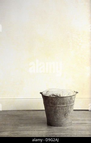 A rusty metal bucket, filled with cloth, placed on a wooden floor Stock Photo