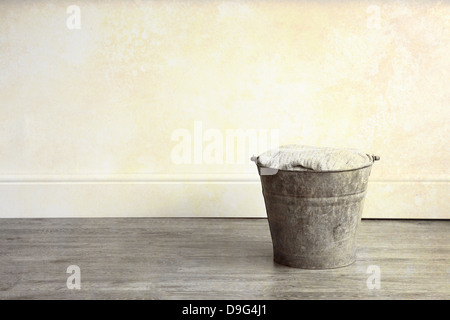 A rusty metal bucket, filled with cloth, placed on a wooden floor Stock Photo