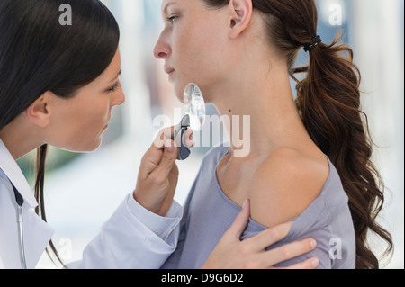 Dermatologist using magnifying glass to examine woman's skin Stock Photo