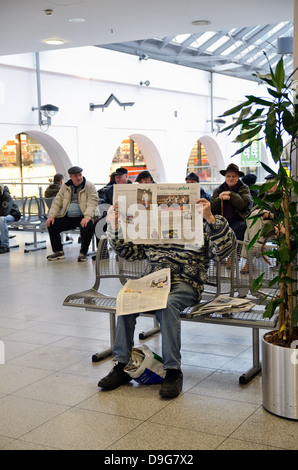 Man reading newspapers, sitting on bench in train station waiting room, Nuremberg, Bavaria, Germany - Jan 2012 Stock Photo