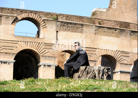 Young man in suit and sunglasses sits by Rome's Coliseum Stock Photo