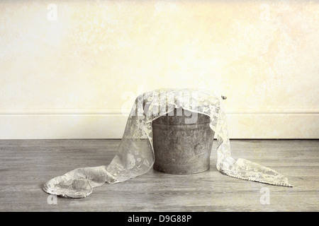 A rusty metal bucket filled with cloth and lace material, placed on a wooden floor Stock Photo