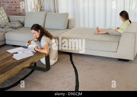 Woman doing paperwork with her daughter using a digital tablet at home Stock Photo