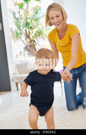 Smiling mother helping her baby to walk Stock Photo