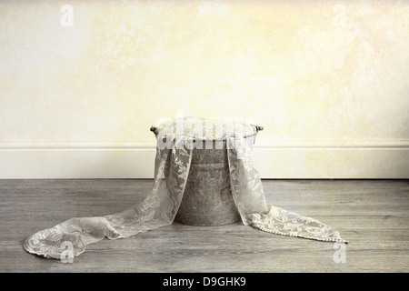 A rusty metal bucket filled with cloth and lace material, placed on a wooden floor Stock Photo