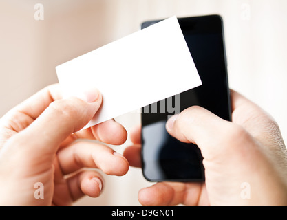 Man holding blank business card and dialing numbers on mobile phone Stock Photo
