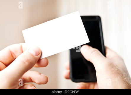 Man holding blank business card and dialing numbers on mobile phone Stock Photo