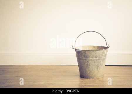 A rusty metal bucket placed on a wooden floor Stock Photo