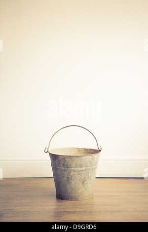 A rusty metal bucket placed on a wooden floor Stock Photo